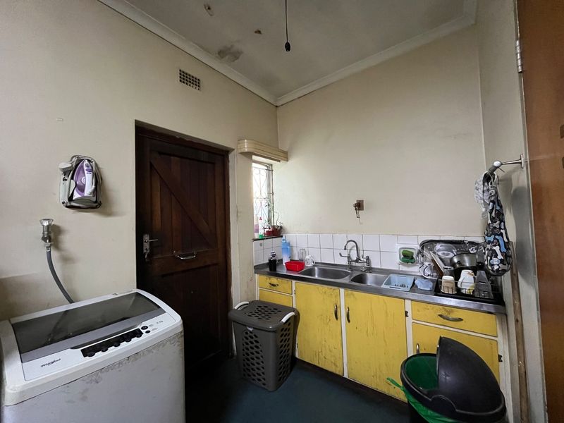 A functional laundry room featuring a stainless steel double sink, fitted cabinetry, and tiled splashback, requiring cosmetic updates to improve its overall condition.