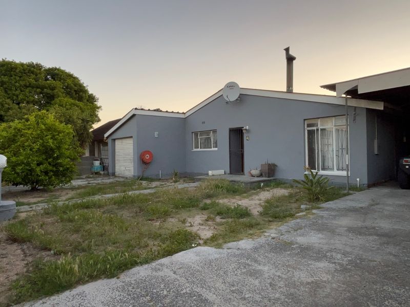 Front elevation of a single-story house featuring a garage, concrete driveway, and established garden area requiring maintenance.