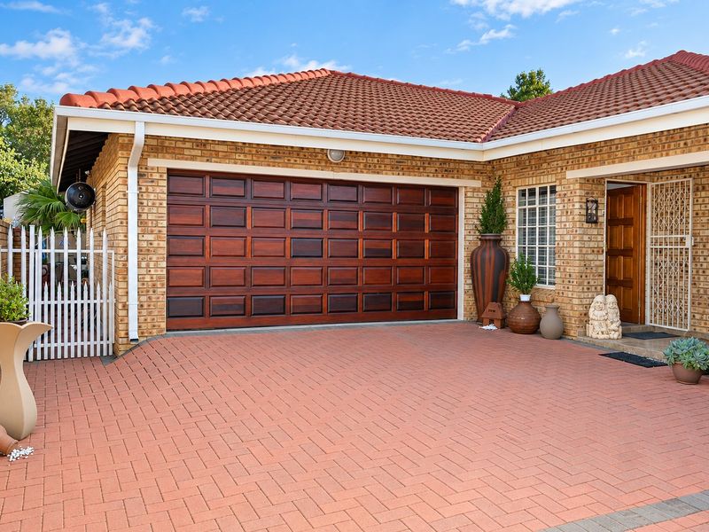Front exterior view of the townhouse featuring a paved driveway, double wooden garage door, and a secure entrance with a security gate.