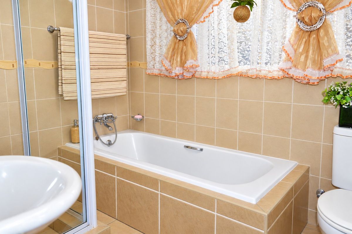 A functional bathroom featuring a built-in bathtub with shower mixer, ceramic tiling throughout, a standard toilet, and a pedestal basin.