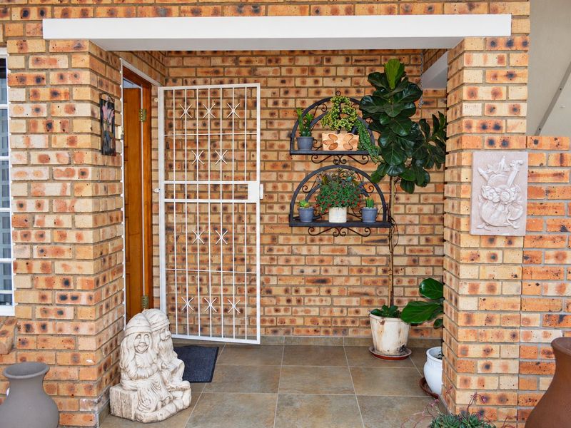 A welcoming entrance area featuring face brick walls, durable tiled flooring, and a secure metal gate leading to the main timber front door.
