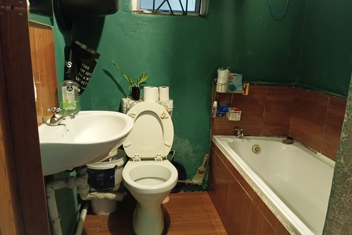 Compact bathroom featuring a pedestal basin, toilet, and bathtub with tiled splashbacks, requiring cosmetic updates and wall repairs.