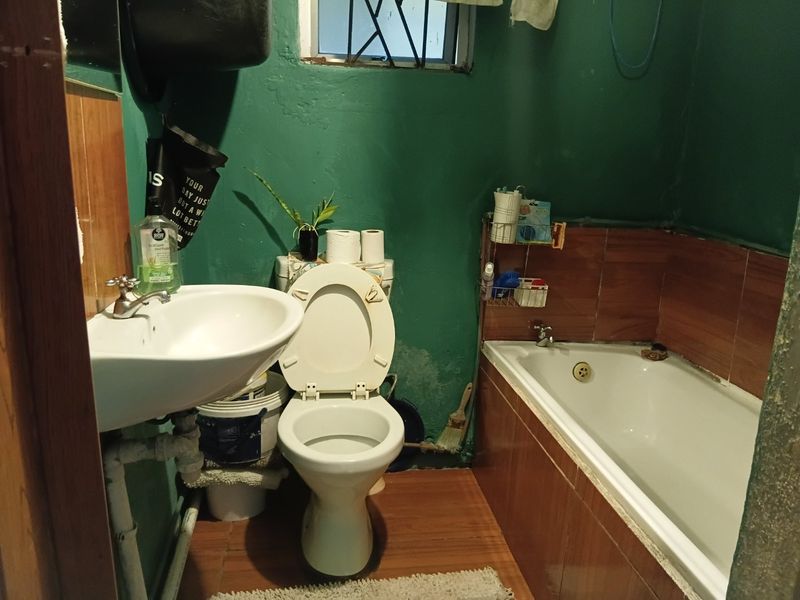 Compact bathroom featuring a pedestal basin, toilet, and bathtub with tiled splashbacks, requiring cosmetic updates and wall repairs.