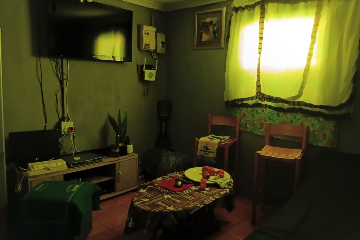 A small living area featuring tiled flooring and wall-mounted electrical infrastructure. The space requires cosmetic updates and improved lighting to enhance its appeal.