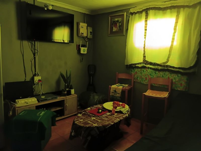 A small living area featuring tiled flooring and wall-mounted electrical infrastructure. The space requires cosmetic updates and improved lighting to enhance its appeal.