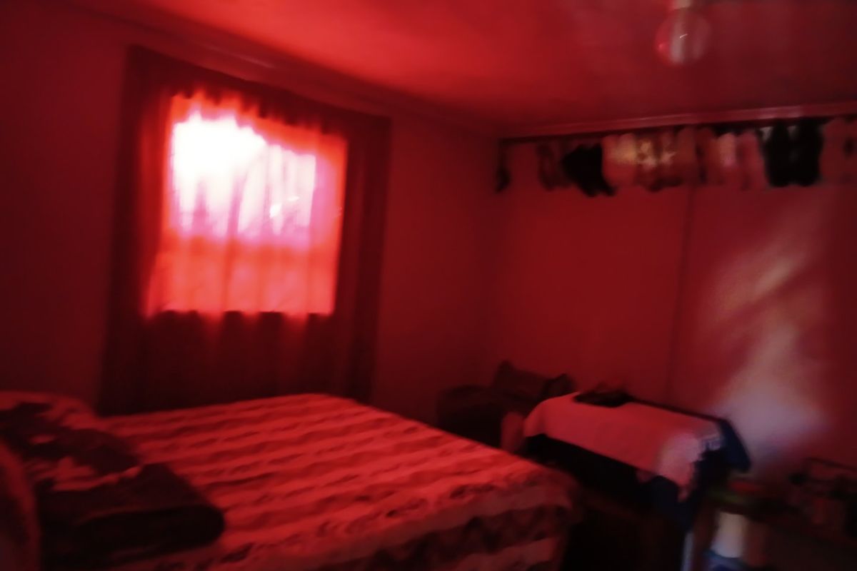 A bedroom interior featuring a window and ceiling light fixture, captured in low-light conditions with a strong red color cast.