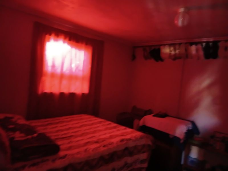 A bedroom interior featuring a window and ceiling light fixture, captured in low-light conditions with a strong red color cast.