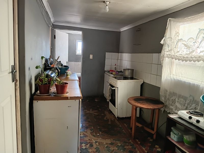 A dated kitchen featuring a freestanding stove, tiled backsplash, and worn flooring, offering significant potential for renovation and modernization.