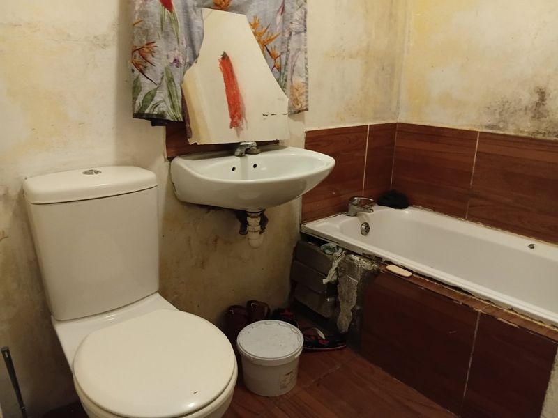 A bathroom in need of significant renovation, featuring a toilet, wall-mounted basin, and bathtub with dated wall finishes and visible signs of wear.