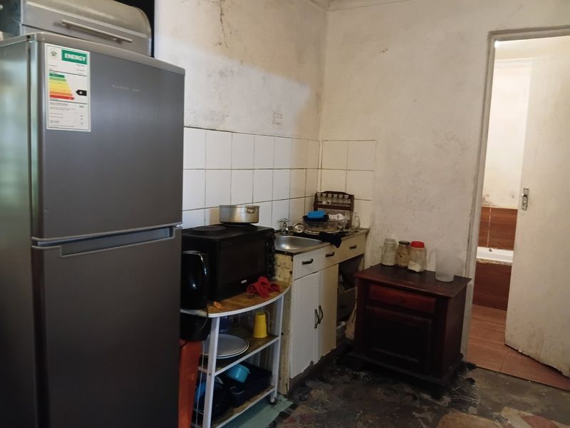 A small, dated kitchen area featuring basic cabinetry, a sink, and tiled backsplash, currently showing significant signs of wear and wall deterioration.
