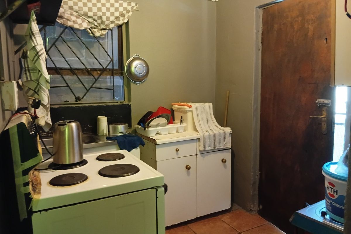 A compact kitchen featuring a freestanding electric stove, built-in cabinetry, and tiled flooring, requiring cosmetic updates to modernize the space.