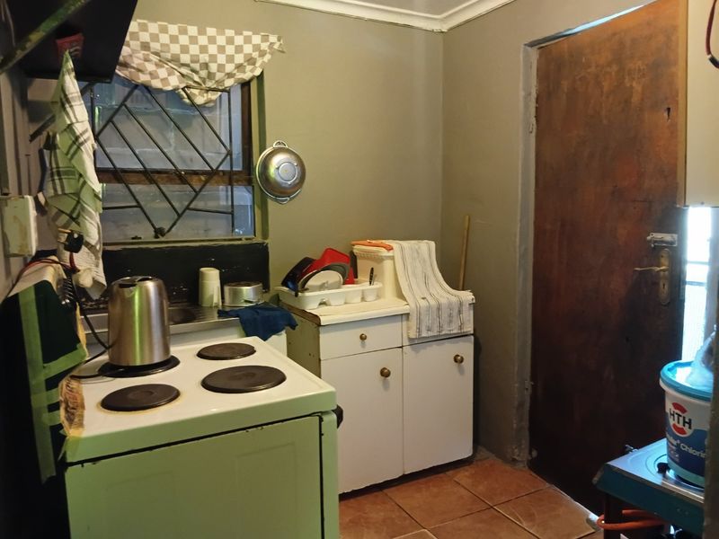 A compact kitchen featuring a freestanding electric stove, built-in cabinetry, and tiled flooring, requiring cosmetic updates to modernize the space.