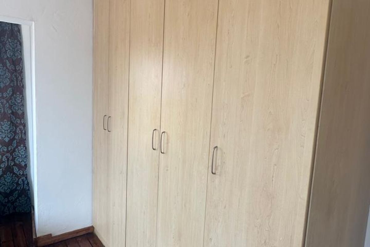 A bedroom featuring light wood-finish built-in cupboards and polished dark wooden flooring.