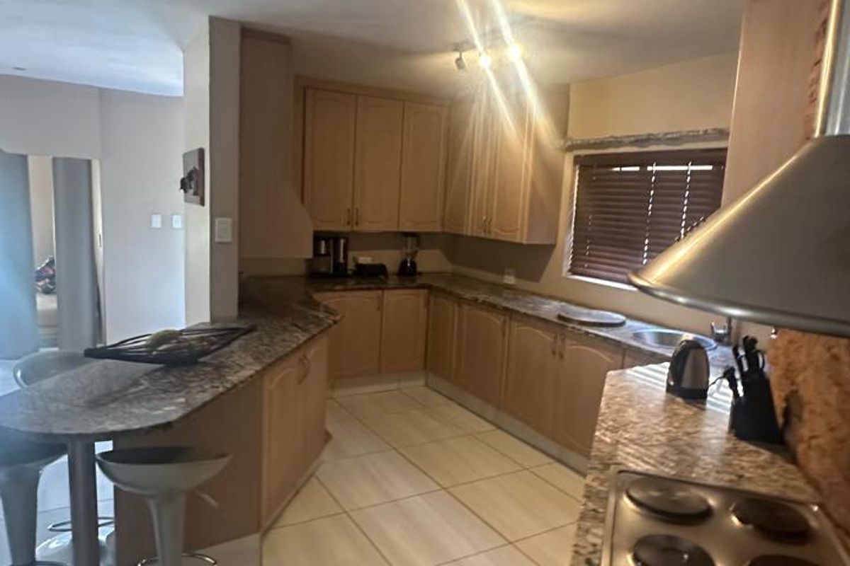 A functional kitchen featuring granite countertops, ample built-in cabinetry, an electric hob with extractor fan, and tiled flooring throughout.