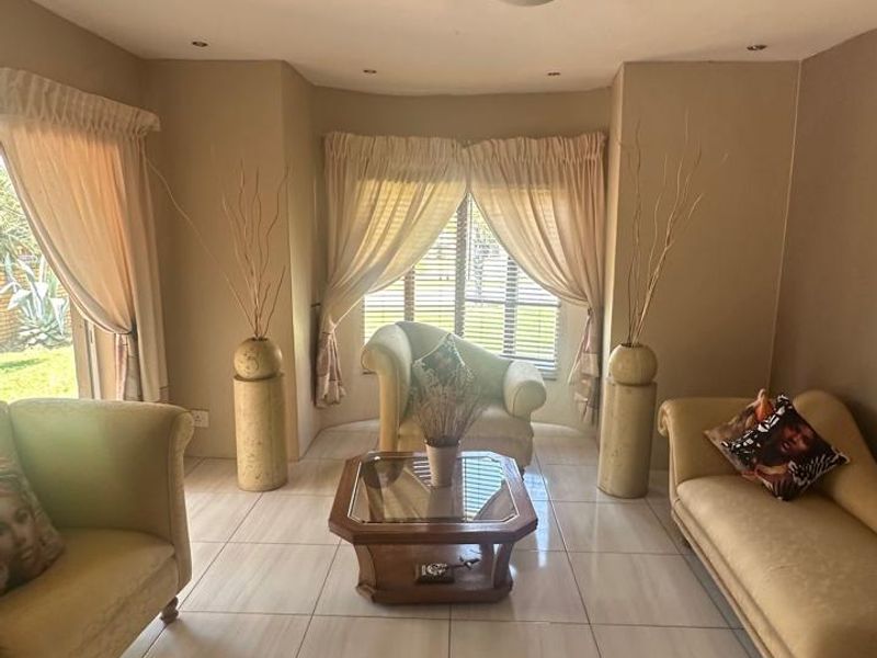 A bright living room featuring large windows, neutral tiled flooring, and a distinctive architectural archway, offering a comfortable and inviting space.