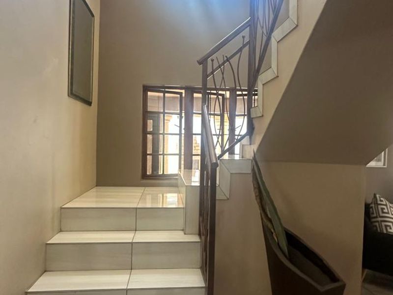 A bright hallway featuring a tiled staircase with a decorative wrought iron balustrade and natural light from clerestory and timber frame windows.