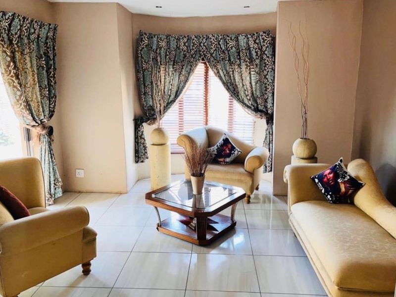 A comfortable living room featuring large format floor tiles and a bay window with venetian blinds, offering a bright and inviting space.