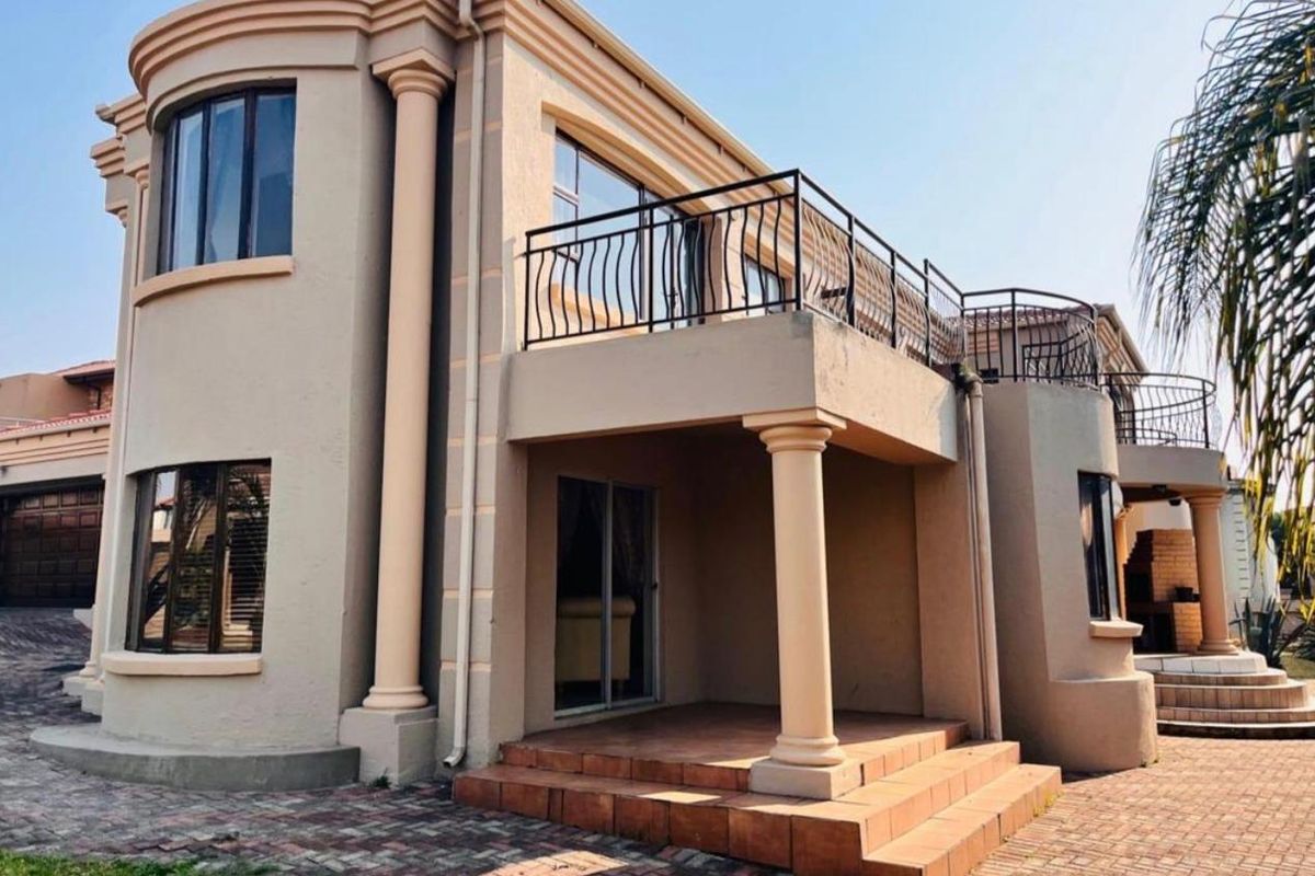 Rear view of a multi-story house featuring a covered patio, an upper-level balcony with wrought iron railings, and classic architectural columns.