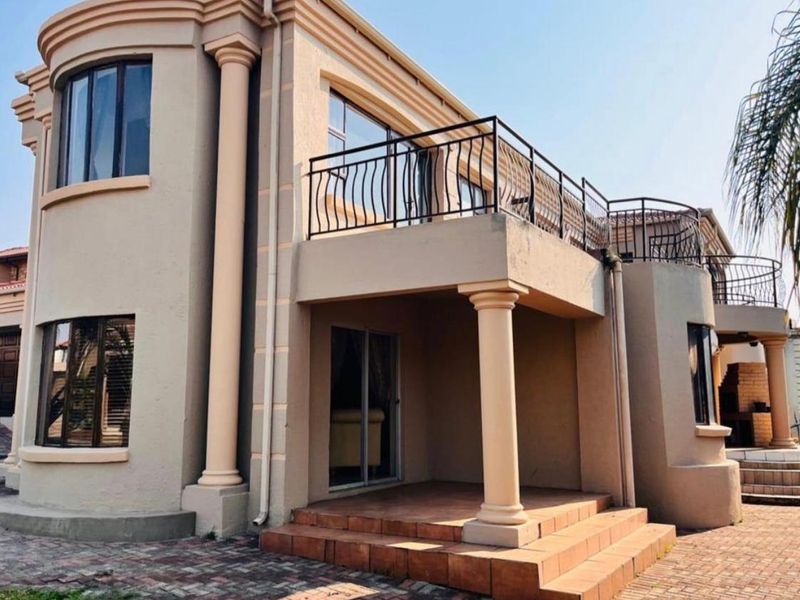 Rear view of a multi-story house featuring a covered patio, an upper-level balcony with wrought iron railings, and classic architectural columns.