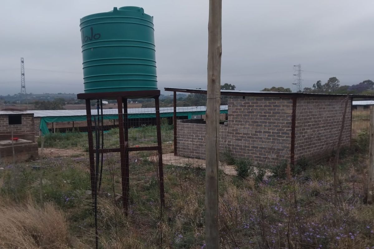 Exterior view of farm outbuildings featuring a water storage tank on a steel stand and brick structures with metal roofing.