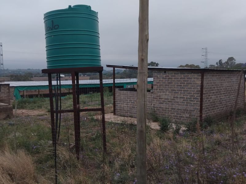 Exterior view of farm outbuildings featuring a water storage tank on a steel stand and brick structures with metal roofing.