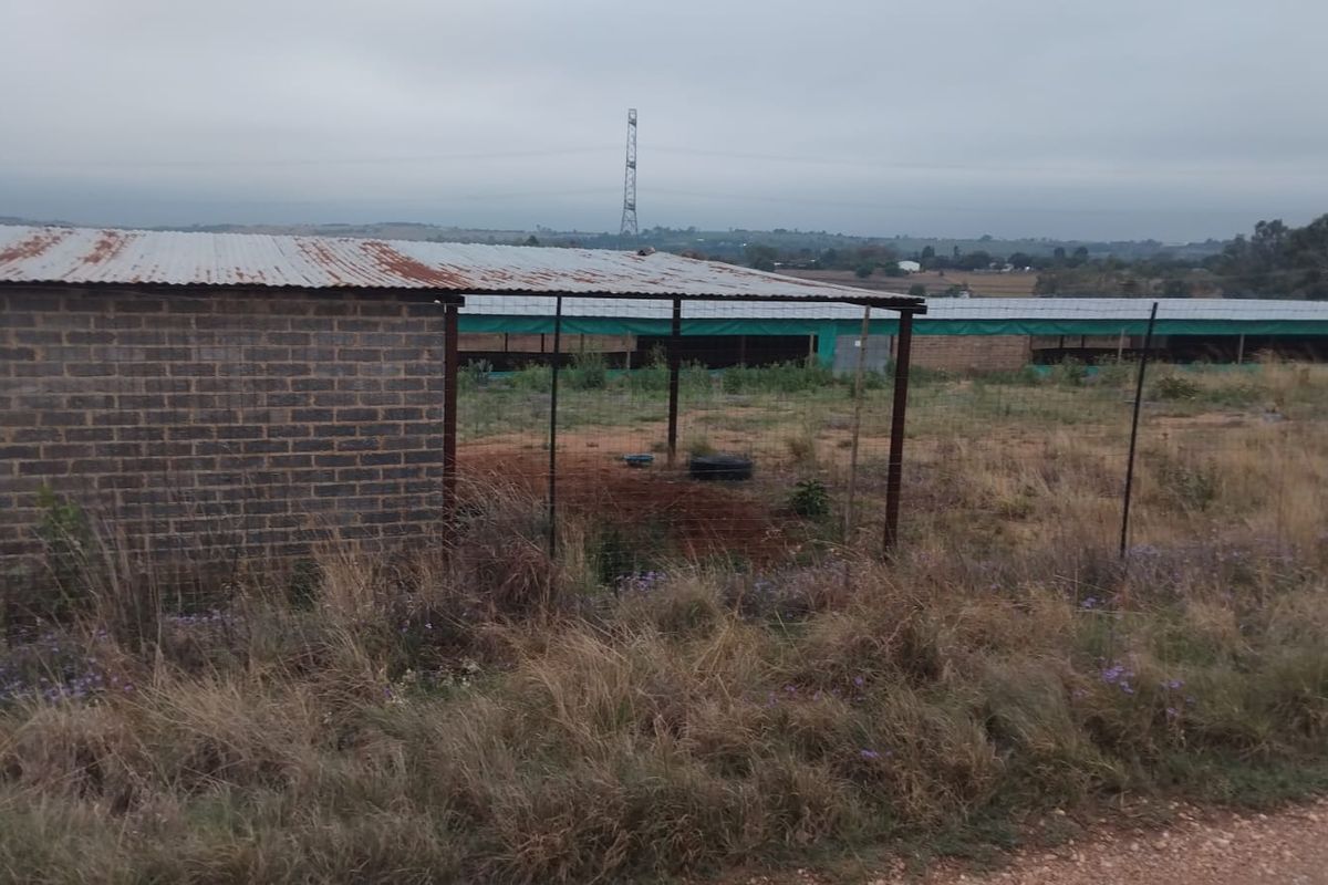 Exterior view of farm outbuildings featuring brick construction and corrugated metal roofing, set within a rural landscape.