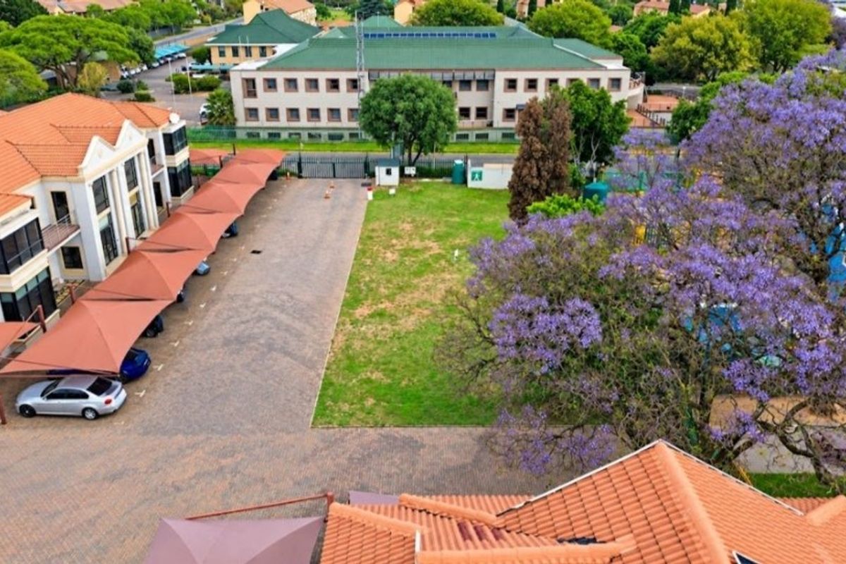 Aerial view of a commercial property featuring a paved parking area with shade cloth carports, a central lawn, and surrounding office buildings.