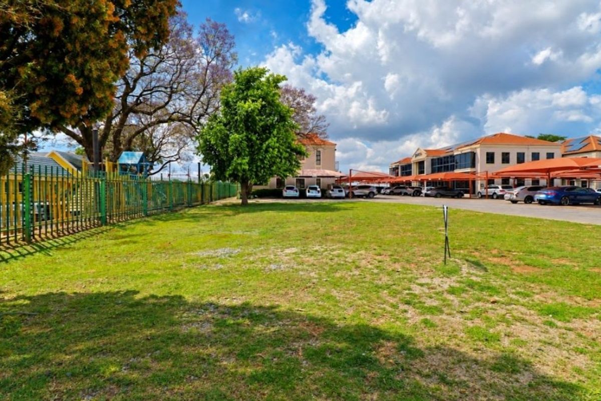 A view of the commercial property grounds featuring a large lawn area, perimeter fencing, and a paved parking lot with shade cloth carports.