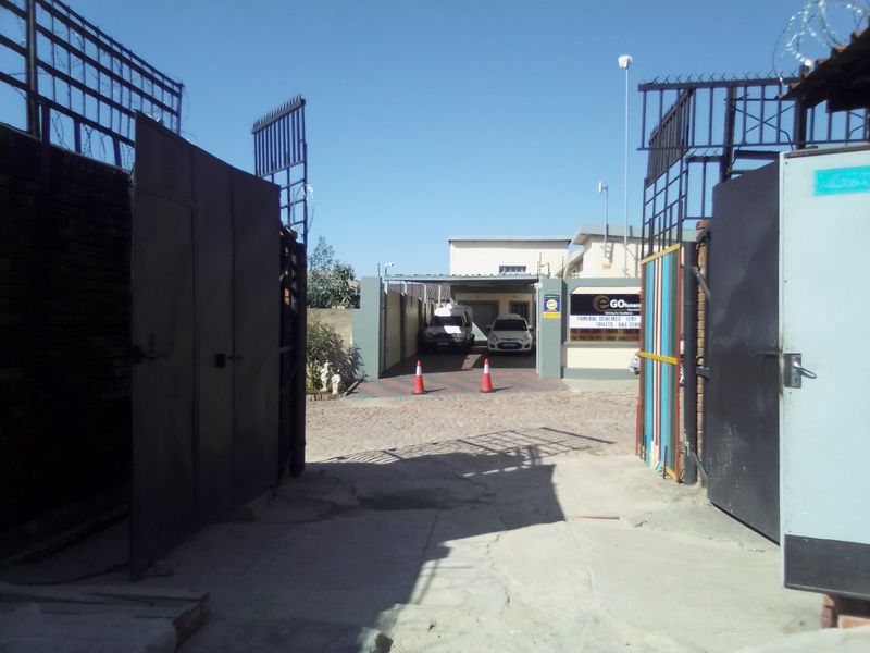 Front entrance view of a commercial property featuring metal security gates, a paved driveway, and a covered parking area.