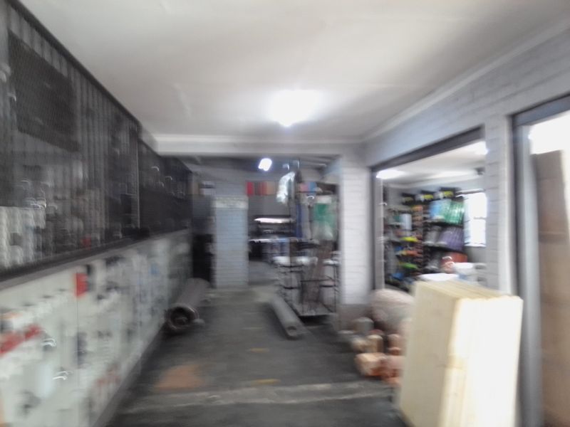 A utilitarian commercial storage or service area featuring concrete floors, exposed brick walls, and security grilles, currently used for inventory storage.