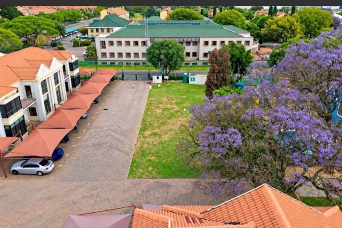 Aerial view of a commercial property featuring a paved parking area with shade cloth carports, a central lawn, and mature landscaping.