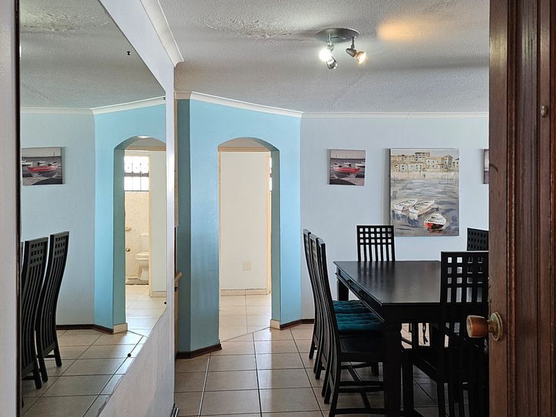 A living and dining area featuring tiled floors, arched doorways, and a ceiling spotlight fixture, showing signs of ceiling water damage.
