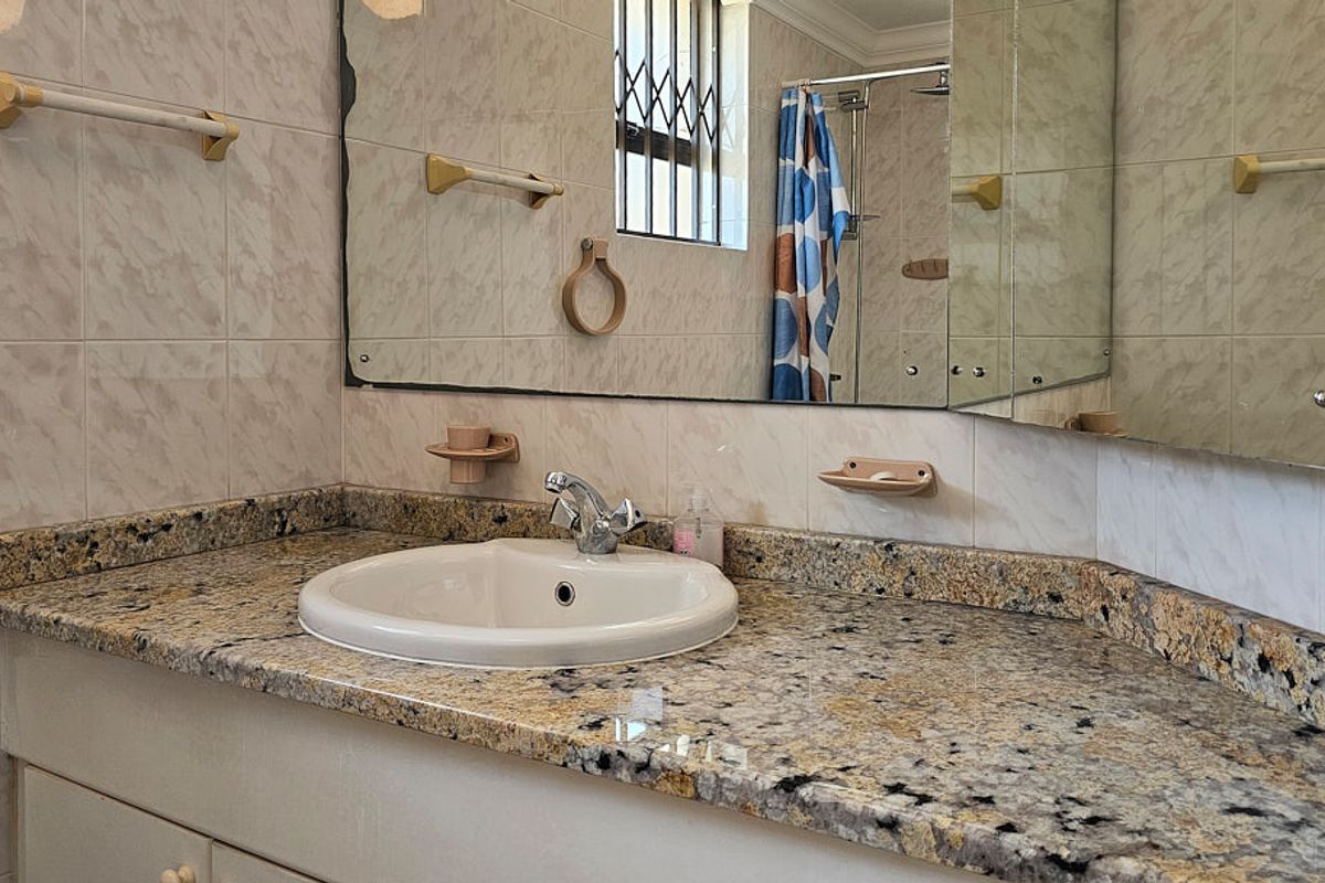 Bathroom featuring a granite vanity countertop with a drop-in basin, tiled walls, and a shower enclosure with security bars on the window.