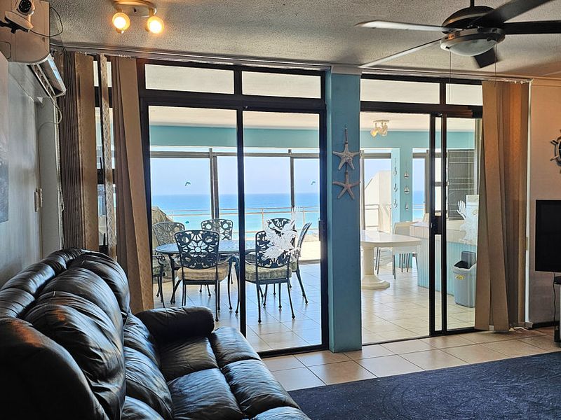 Spacious living area featuring tiled flooring, ceiling fan, and large sliding glass doors opening onto a balcony with ocean views.
