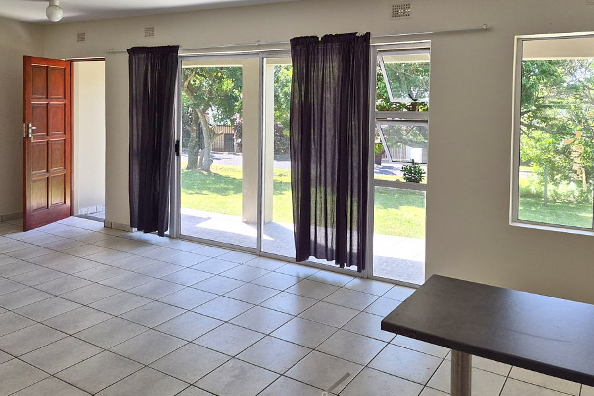 Spacious, light-filled living area featuring neutral tiled flooring, large sliding glass doors providing garden access, and ample natural light through aluminium-framed windows.