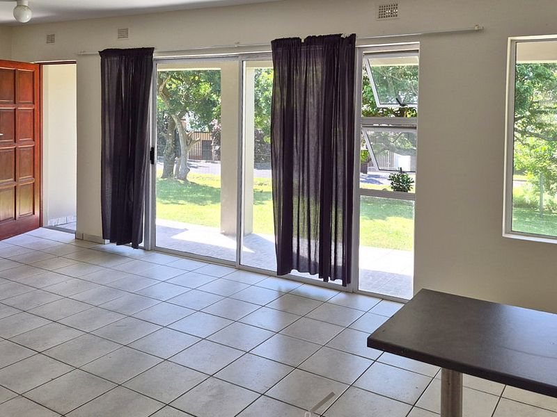 Spacious, light-filled living area featuring neutral tiled flooring, large sliding glass doors providing garden access, and ample natural light through aluminium-framed windows.