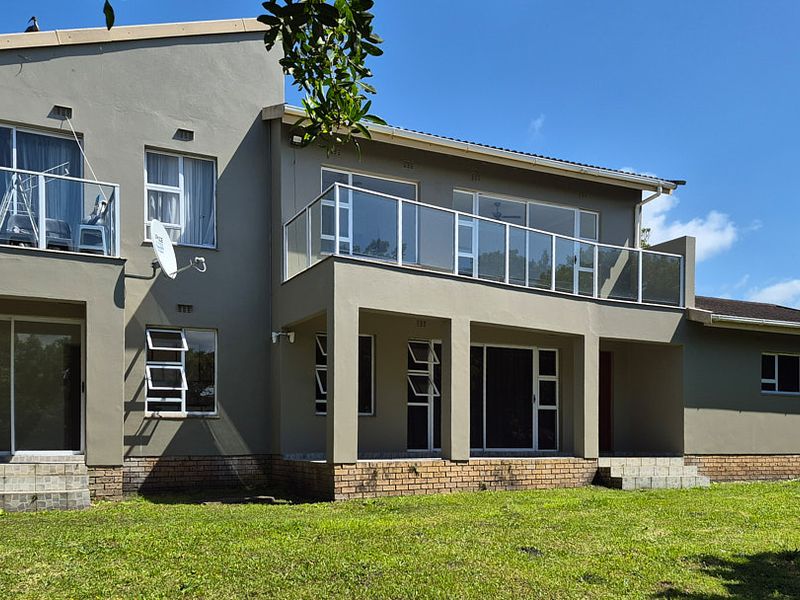 Rear elevation of a multi-story house featuring a spacious balcony with glass balustrades, sliding doors, and a well-maintained lawn area.