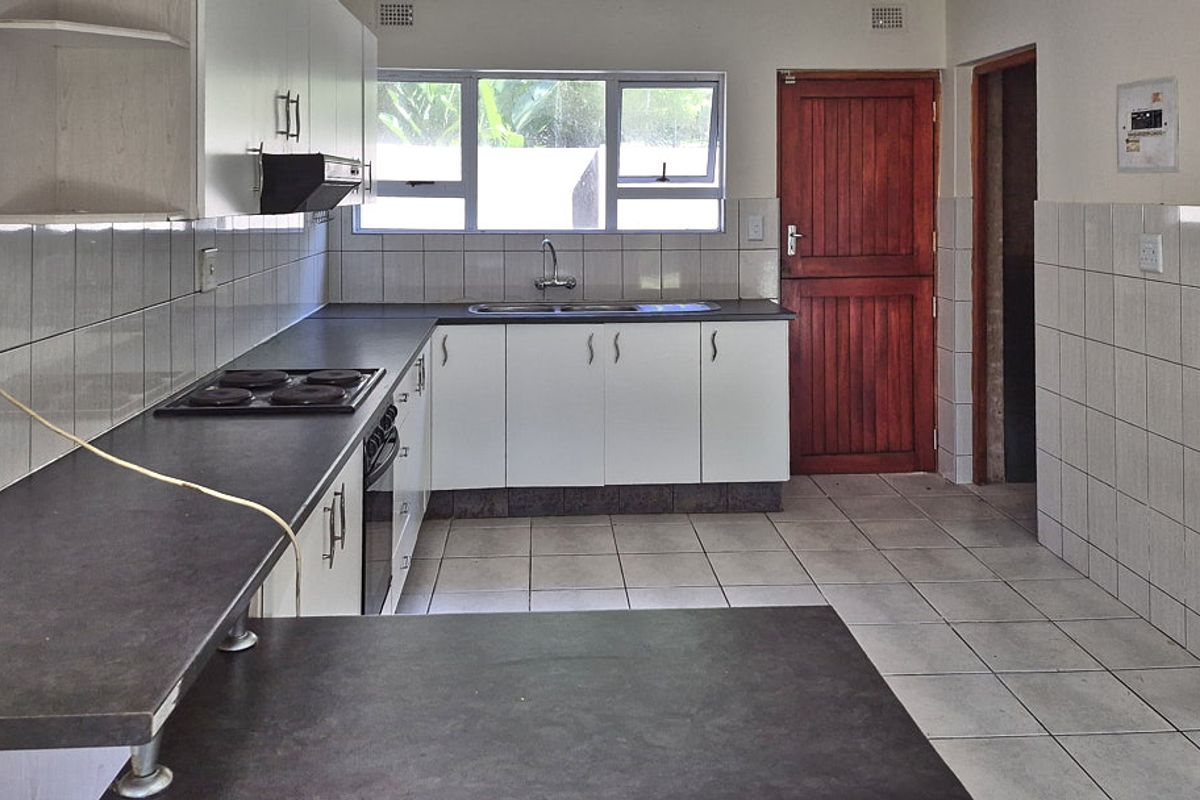 A functional kitchen featuring white cabinetry, dark laminate countertops, an integrated electric hob and oven, and tiled flooring throughout.