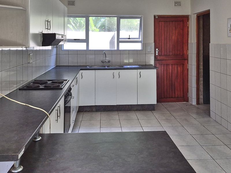 A functional kitchen featuring white cabinetry, dark laminate countertops, an integrated electric hob and oven, and tiled flooring throughout.