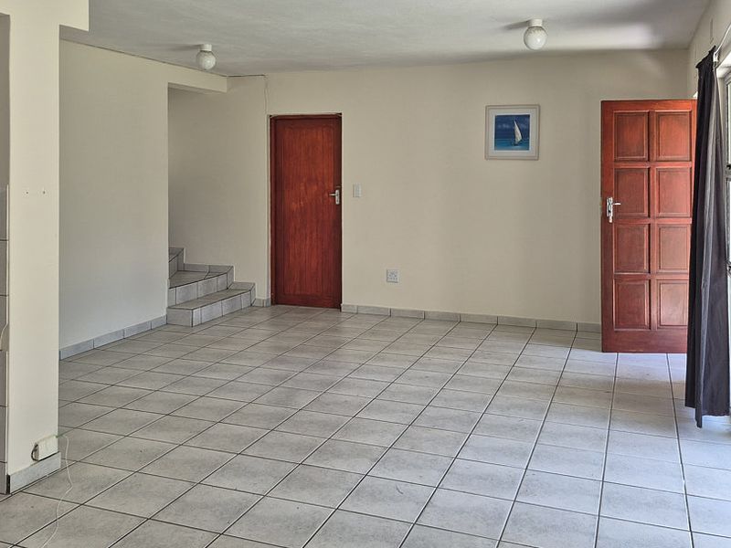 An open-plan living area featuring neutral tiled flooring, wooden doors, and a small tiled staircase, offering a blank canvas for interior design.