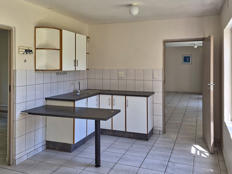 A functional, empty kitchen featuring white cabinetry, laminate countertops, a breakfast bar, and tiled flooring, offering a blank canvas for modern renovation.