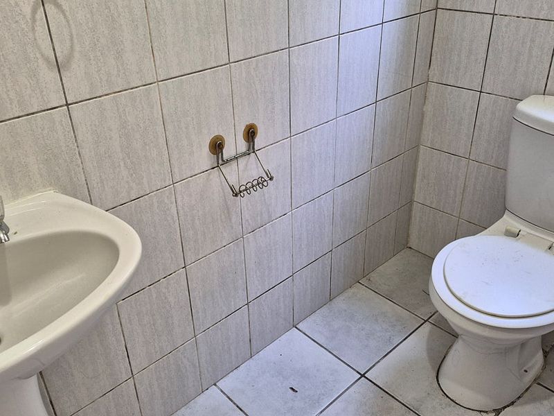 A compact bathroom featuring a pedestal washbasin and a standard toilet, finished with neutral ceramic wall and floor tiles.