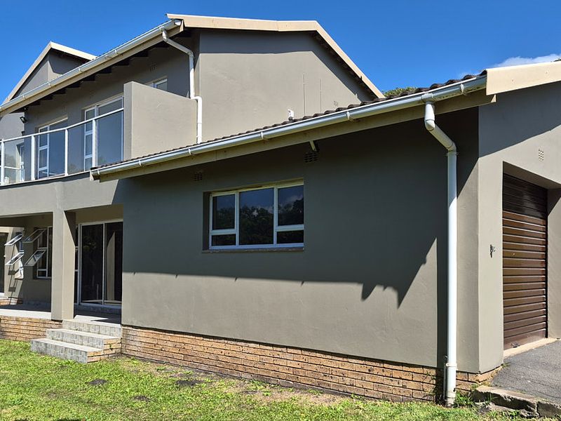 A modern double-story house featuring a double garage, a spacious upper-level balcony with glass balustrades, and a well-maintained exterior facade.