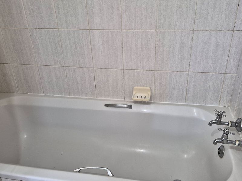 A functional bathroom featuring a standard bathtub with wall-mounted faucets and tiled surround, offering a blank canvas for modern renovation.