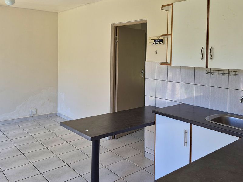 A functional kitchen area featuring tiled flooring, built-in cabinetry, a breakfast bar, and a stainless steel sink, requiring some cosmetic updates.