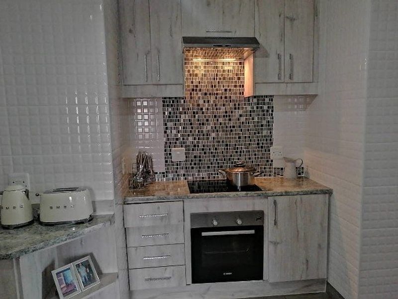 Compact kitchen featuring light wood-grain cabinetry, granite countertops, a mosaic tile backsplash, and integrated stainless steel appliances including an oven and hob.