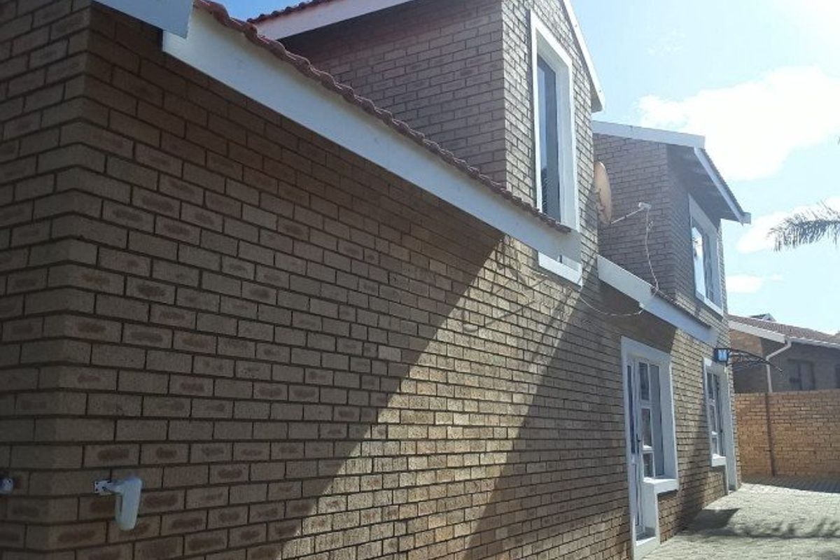 A side view of a double-story face brick house featuring a tiled roof and paved exterior area.