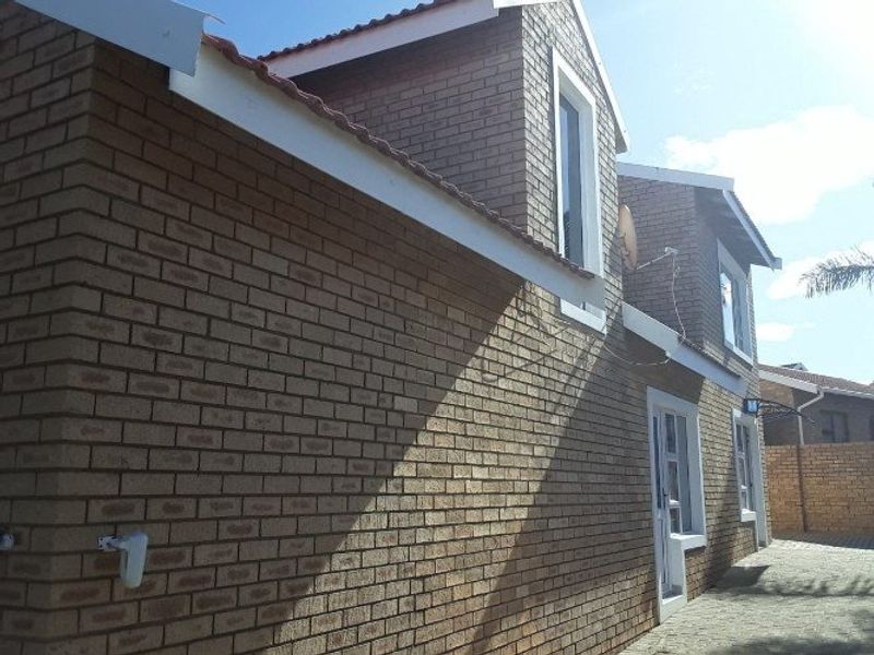 A side view of a double-story face brick house featuring a tiled roof and paved exterior area.