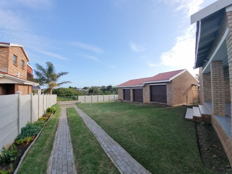 Spacious rear garden area featuring a triple garage, paved driveway, and secure boundary walling.
