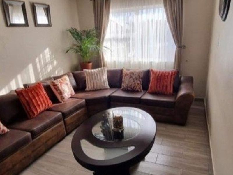 A comfortable living room featuring wood-look laminate flooring, neutral wall tones, and large windows with installed curtain rails.